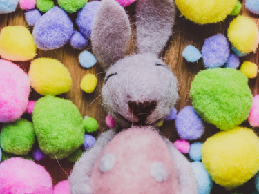 Bilde av en tovet hare som ligger rundt fargerike egg