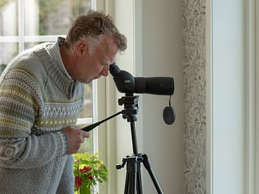 Bilde av huseier som ser ut vinduet med kikkert