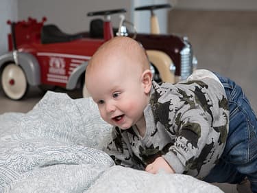 Bilde av minstemann i huset som leker med en dyne på stuegulvet